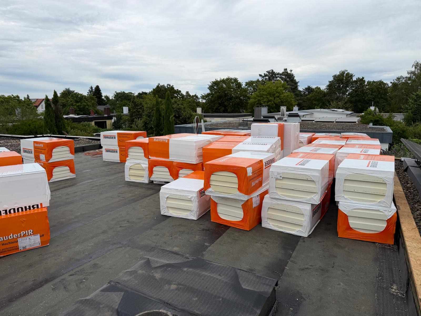 Gestapelte Dämmplatten der Marke Bauder auf einer Flachdachfläche vor bewölktem Himmel